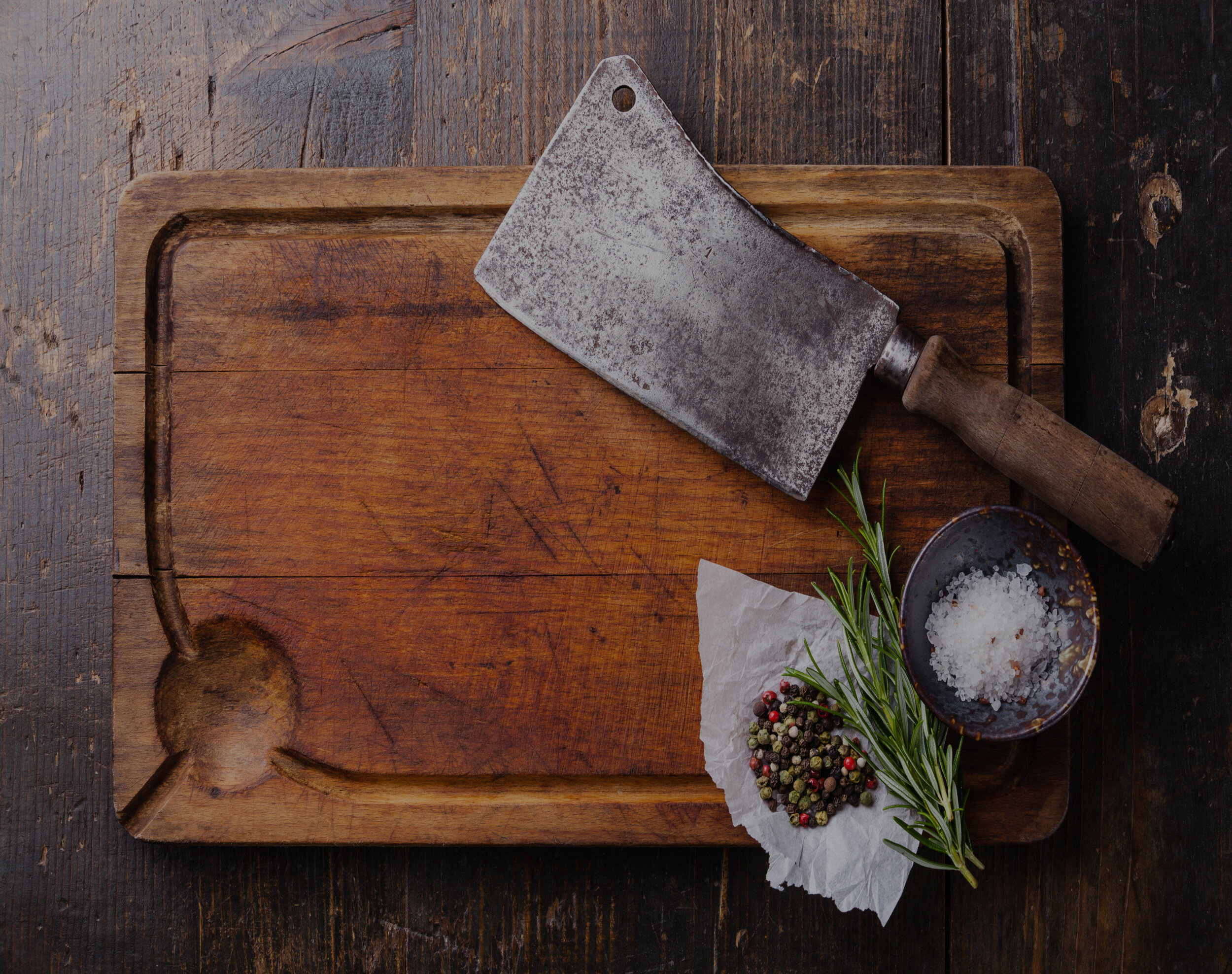 Chopping board, seasonings and meat cleaver on dark wooden background
